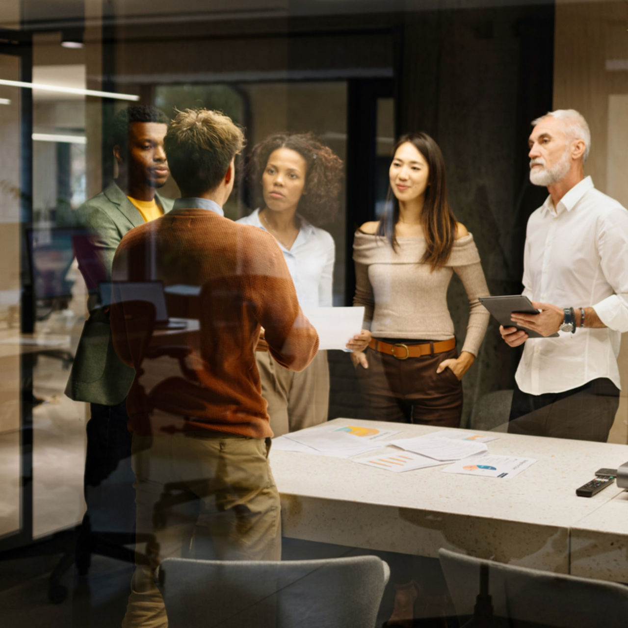 A group of researchers in a range of ages, genders, and races are having a discussion near a table scattered with papers. 